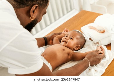 A joyful father interacts with his smiling baby during a tender moment on a changing table, fostering connection and playfulness. Happy diversity family and newborn bathing concept. - Powered by Shutterstock