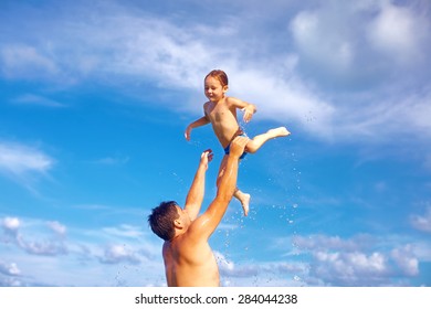 joyful father and son having fun in water on tropical beach
