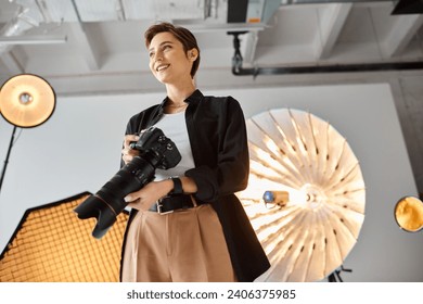 joyful female photographer in casual attire with camera in her hands smiling and looking away - Powered by Shutterstock