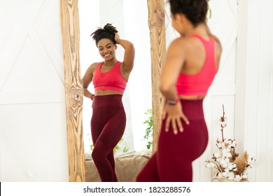 Joyful Fit Black Lady After Successful Weight Loss Posing Near Mirror Looking At Reflection Standing At Home. Weight-Loss, Slimming Motivation Concept. Selective Focus