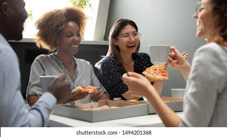 Joyful friendly multicultural business team people having fun eating pizza together in office, happy diverse workers staff group talk laugh share lunch food meal enjoy party at work break meeting