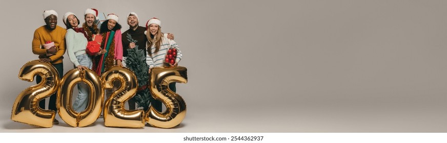 Joyful friends holding Christmas ornaments and gift boxes while celebrating 2025 New Year on studio background - Powered by Shutterstock