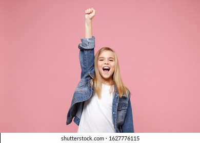 Joyful funny little blonde kid girl 12-13 years old in denim jacket isolated on pastel pink background children portrait. Childhood lifestyle concept. Mock up copy space. Rising hand, clenching fist