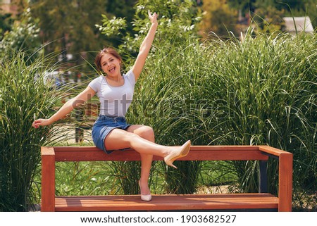 Joyful, funny teenage girl fooling around on a bench in a city park.