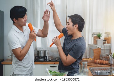 Joyful Gay Couple Singing And Dancing During Breakfast In Kitchen, Use Carrot Instead Of Microphone