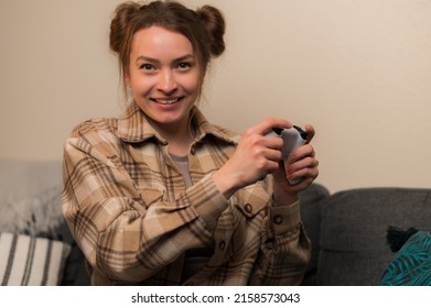 Joyful girl gamer in a plaid shirt with a joystick plays video games. Virtual reality, cyberspace, youth culture, communication with friends, hobby, hobby, electronics, leisure.