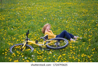 Freudenmädchen - Teenager im Alter von 16-17 Jahren liegt auf grünem Gras unter gelben Lüstern, neben ihr ist Fahrrad. Radfahren im Freien, Harmonie, Energie der Natur, Entspannung, Freiheit. Aktive gesunde Lebensweise