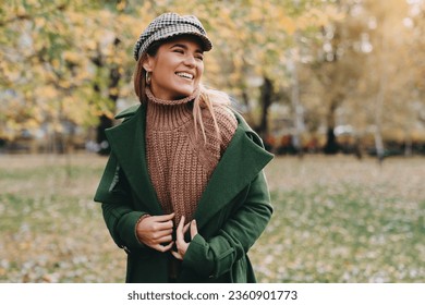 Joyful girl in warm clothing smiling at public park. Young student girl taking a walk outside of her college campus during the nice autumn day.