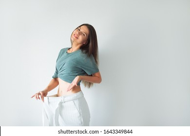 The joyful girl who lost weight points to her former huge pants. Woman Losing Weight After Diet, Slim Down, Burning Fat and Flat Waist. Thin Girl Show Weight Loss and Old Big Jeans. Too Large Pants. 