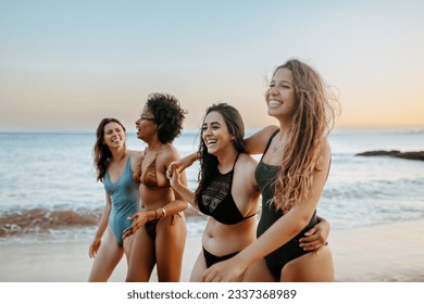 Joyful girlfriends in swimwear walking on beach at sunset and enjoying free time together, laughing and chatting, having promenade during their summer vacation - Powered by Shutterstock