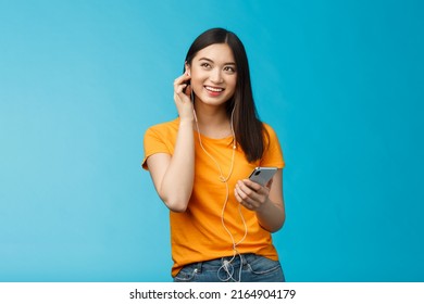 Joyful Good-looking Asian Woman Look Up Delighted, Hold Smartphone Plug-in Earphone Smiling Satisfied Good Sound Quality, Enjoy Listening Music Stand Blue Background Enthusiastic Upbeat