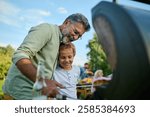 Joyful grandfather embraces his grandson while grilling outdoors at a family barbecue, sharing smiles, hugs, and care in a heartwarming scene. Greenery adds to the festive atmosphere