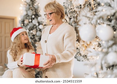 A joyful grandmother and granddaughter exchange a Christmas gift in a beautifully decorated room, symbolizing love, joy, and togetherness during the festive holiday season. - Powered by Shutterstock