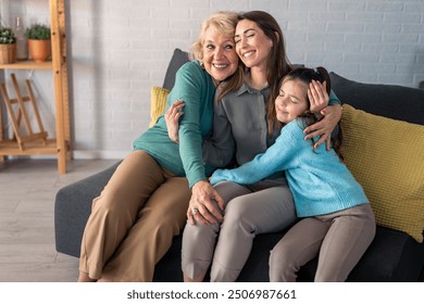 A joyful grandmother, her daughter, and granddaughter share a snug hug on a cozy sofa, radiating happiness in a well-lit living room. - Powered by Shutterstock