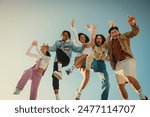 Joyful group of friends jumping together outdoors, capturing happy and fun moments in the sunshine. The sky in the background enhances their exhilaration.