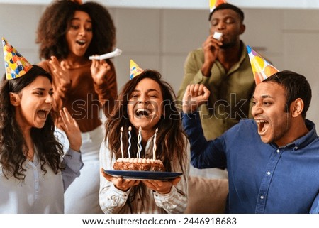 A joyful group of multiracial friends sings the birthday song to a friend holding a cake with lit candles, celebrating together