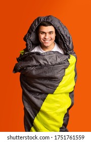 Joyful Guy Hiker Wrapped In Colorful Sleeping Bag Over Orange Studio Background