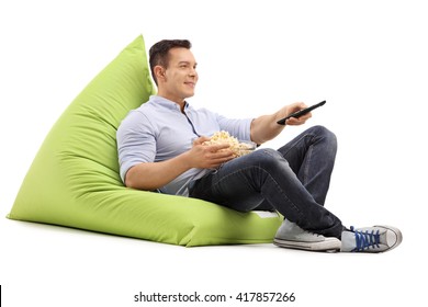 Joyful Guy Watching TV Seated On A Green Beanbag And Eating Popcorn Isolated On White Background