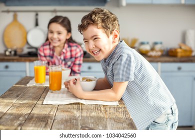 So joyful. Handsome delighted little dark-haired boy laughing and having healthy breakfast with his sister and the girl smiling in the background - Shutterstock ID 1034042560