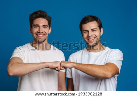 Joyful handsome friends guys smiling and fist bumping isolated over blue background