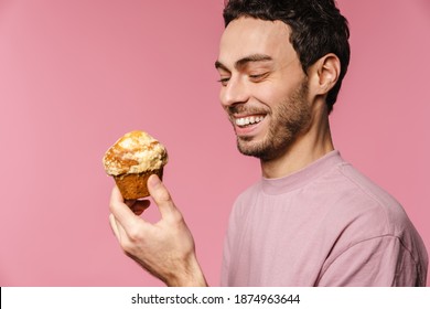 Joyful handsome guy laughing while posing with muffin isolated over pink background