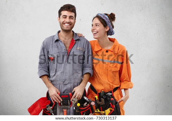 Joyful handyman being glad to repair car,\
recieves support from wife, rejoice promotion at work. Service\
workers have many clients. Smiling woman and man work of bilduing\
team, construct\
something