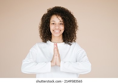 Joyful happy african american young woman joined hands, thanking for good luck, isolated on brown studio background. Girl smiling female prayer waiting for miracle                               