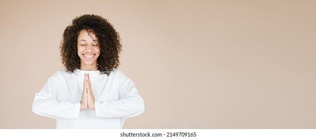Joyful happy african american young woman joined hands, thanking for good luck, isolated on brown studio background. Girl smiling female prayer waiting for miracle                                     
