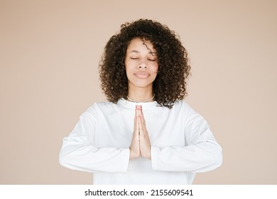 Joyful happy african american young woman joined hands, thanking for good luck, isolated on brown studio background. Girl smiling female prayer waiting for miracle	                               