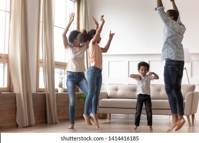 Joyful Happy African Family Having Fun Jumping In Living Room Together, Active Black Parents And Little Cute Kids Dancing At Home, Mixed Race Mom Dad With Small Kids Laughing Enjoy Leisure Activity