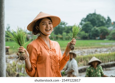 A joyful and happy farmer beams with pride as he showcases rice seedlings in lush, fertile fields - Powered by Shutterstock