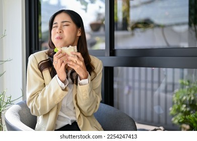 Joyful, happy and hungry millennial Asian businesswoman or female office worker enjoying with her yummy sandwich at the cafe. urban lifestyle concept - Powered by Shutterstock