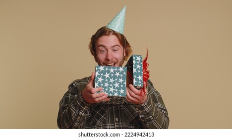 Joyful Happy Young Man Opening Gift Box, Unwrapping Birthday Surprise And Expressing Great Happiness Amazement, Satisfied With Best Present Bonus. Young Guy Boy Isolated On Beige Studio Background