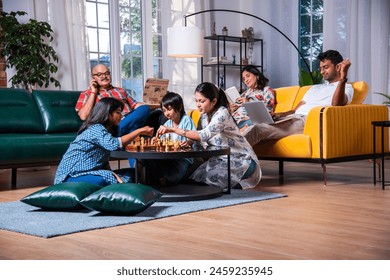 Joyful Indian asian kids playing chess in living room with senior grandparents and parents at home - Powered by Shutterstock