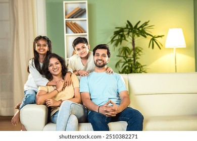 Joyful Indian family of four enjoying quality time at home, parents and kids sitting on the sofa, laughing and playing together, capturing happy moments of family bonding and love - Powered by Shutterstock