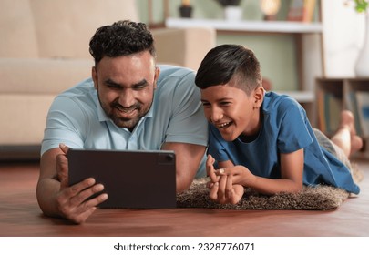 joyful indian father with son using digital tablet while lying on floor at home - concept of weekend holiday, Modern parenting and Digital entertainment - Powered by Shutterstock