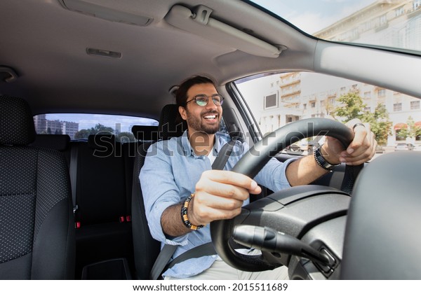 Joyful\
indian man driving car, shot from dashboard, going on trip during\
summer vacation, copy space. Happy middle-eastern guy in casual\
outfit and glasses driving his brand new nice\
car