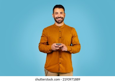 Joyful Italian Guy Holding Modern Smartphone Looking At Camera Screen On Blue Studio Background