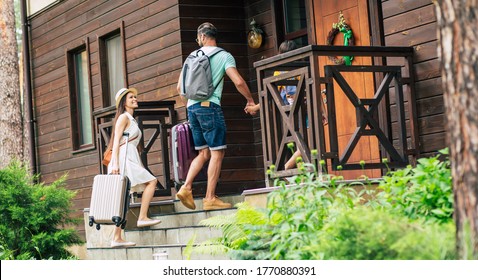 Joyful Journey. A Photo Of A Smiling Travelling Summer Dressed Family With Suitcases And Backpacks Coming To The Hotel, Going Up Stairs, Father And Mother Looking At Each Other.