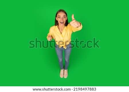 Joyful Lady Gesturing Thumbs Up Approving Offer Smiling Looking At Camera Standing Posing Over Green Studio Background. I Like It, Approval Concept. High Angle Shot