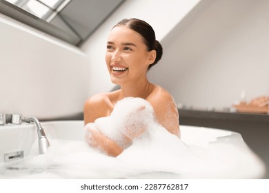 Joyful Lady Washing Body Covered With Foam Sitting In Bathtub And Taking Bath At Home, Smiling Looking Aside. Female Enjoying Bathing In Bathroom. Beauty And Wellbeing Concept - Powered by Shutterstock