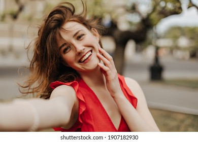 Joyful lady with wavy hair in red clothes taking photo and smiling outside. Cool woman with brown hairstyle in bright outfit posing outdoors.. - Powered by Shutterstock