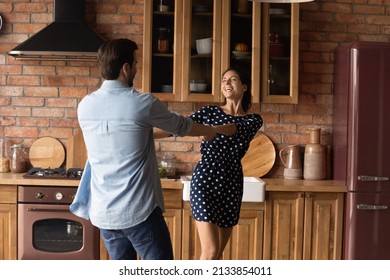 Joyful Laughing Millennial Married Couple Dancing To Music Together In Old Fashioned Kitchen, Celebrating Moving Into Own House, Enjoying Carefree Leisure Weekend Pastime Activity Together At Home.