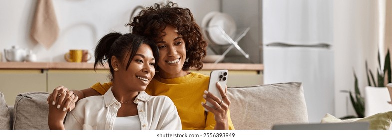 A joyful lesbian couple relaxes on a sofa, sharing laughter while looking at a phone, banner - Powered by Shutterstock