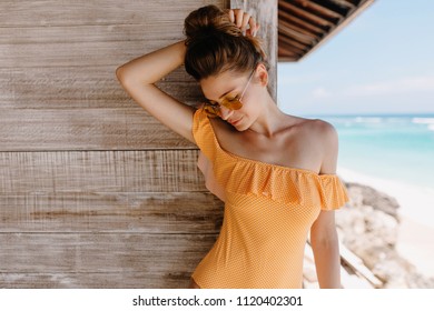 Joyful lightly-tanned girl touching her hair while resting at resort. Outdoor photo of beautiful european woman in orange attire enjoying good day at ocean beach. - Powered by Shutterstock