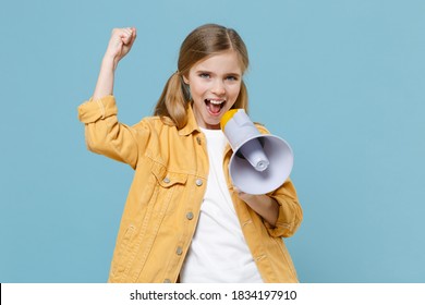 Joyful little blonde kid girl 12-13 years old in yellow jacket posing isolated on pastel blue background. Childhood lifestyle concept. Mock up copy space. Screaming in megaphone doing winner gesture