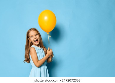 Joyful little girl in a summer dress holding a yellow balloon against a vibrant blue background - Powered by Shutterstock