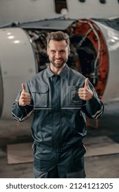 Joyful man aircraft maintenance engineer giving thumbs up and smiling while standing near airplane