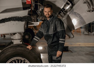 Joyful Man Aviation Maintenance Technician Holding Wrench And Smiling While Repairing Aircraft Wheel At Repair Station