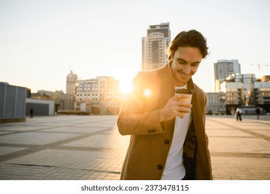 Joyful man in coat looking at disposable cup against sunset in city	 - Powered by Shutterstock